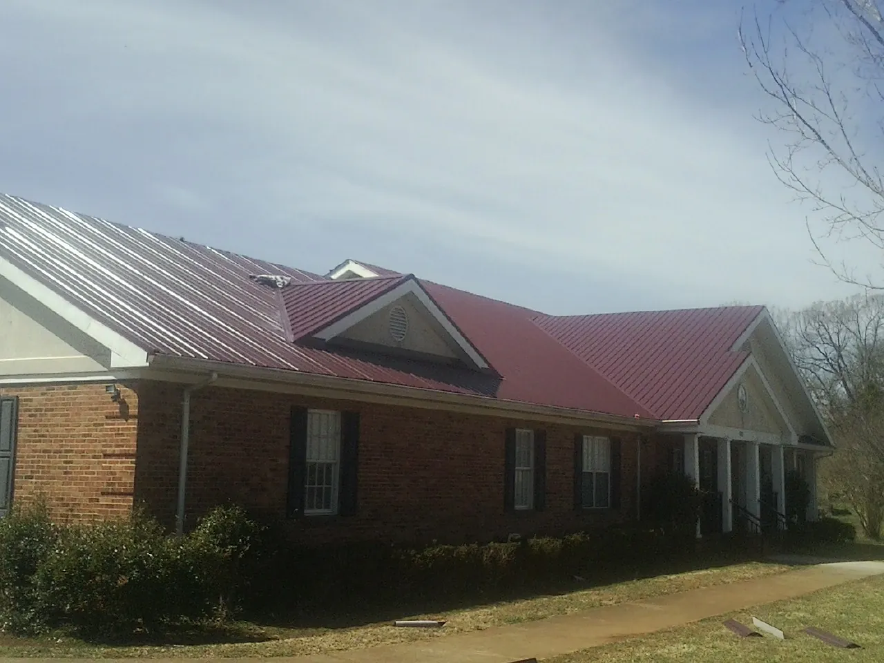 Red metal roof with gabled entries on a long brick building, from a Hail Damage Roof Repair job in Haverford