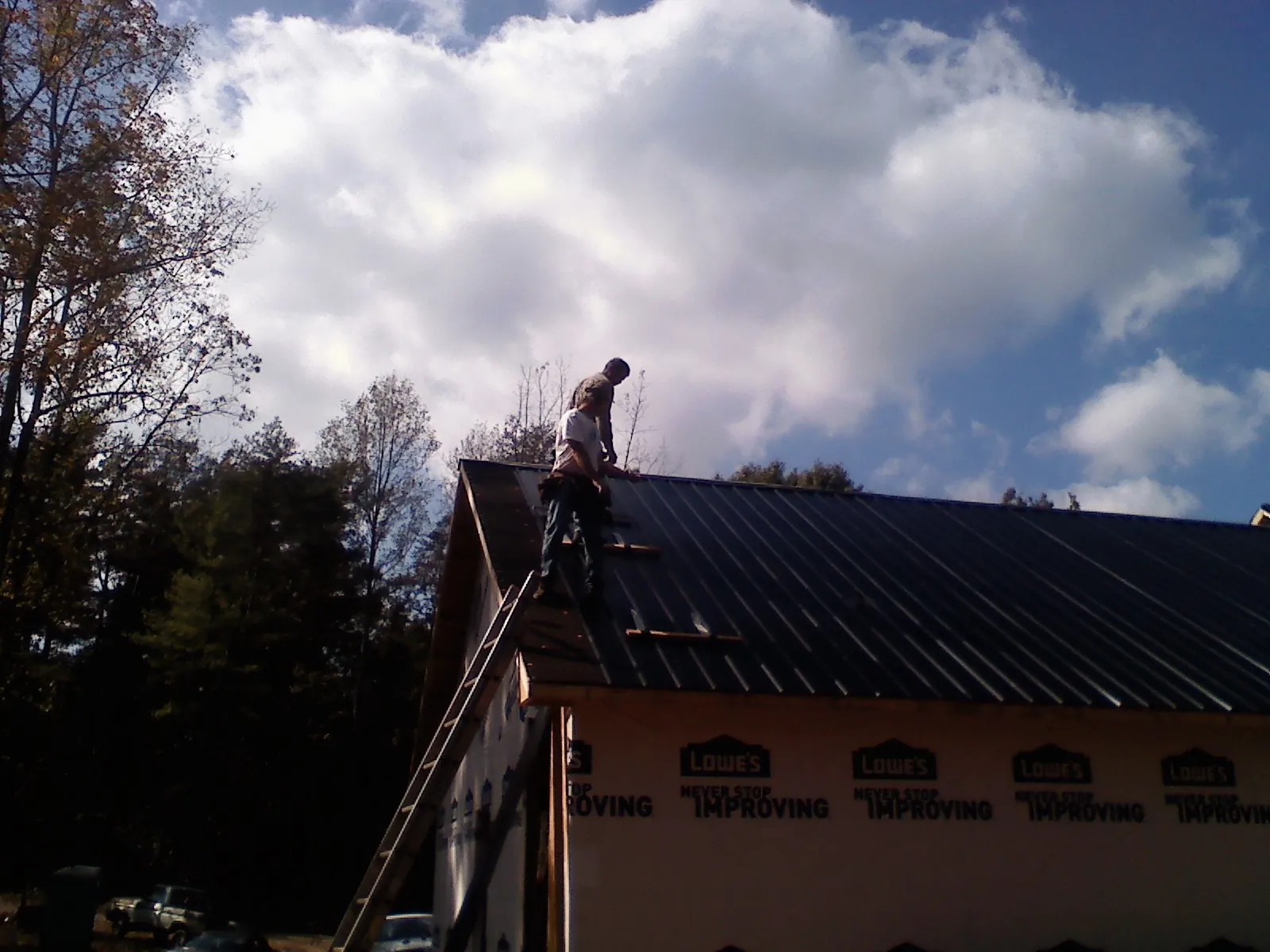 Roofer fastening dark metal panels high against a cloudy sky, from a Roof Inspection job in Haverford