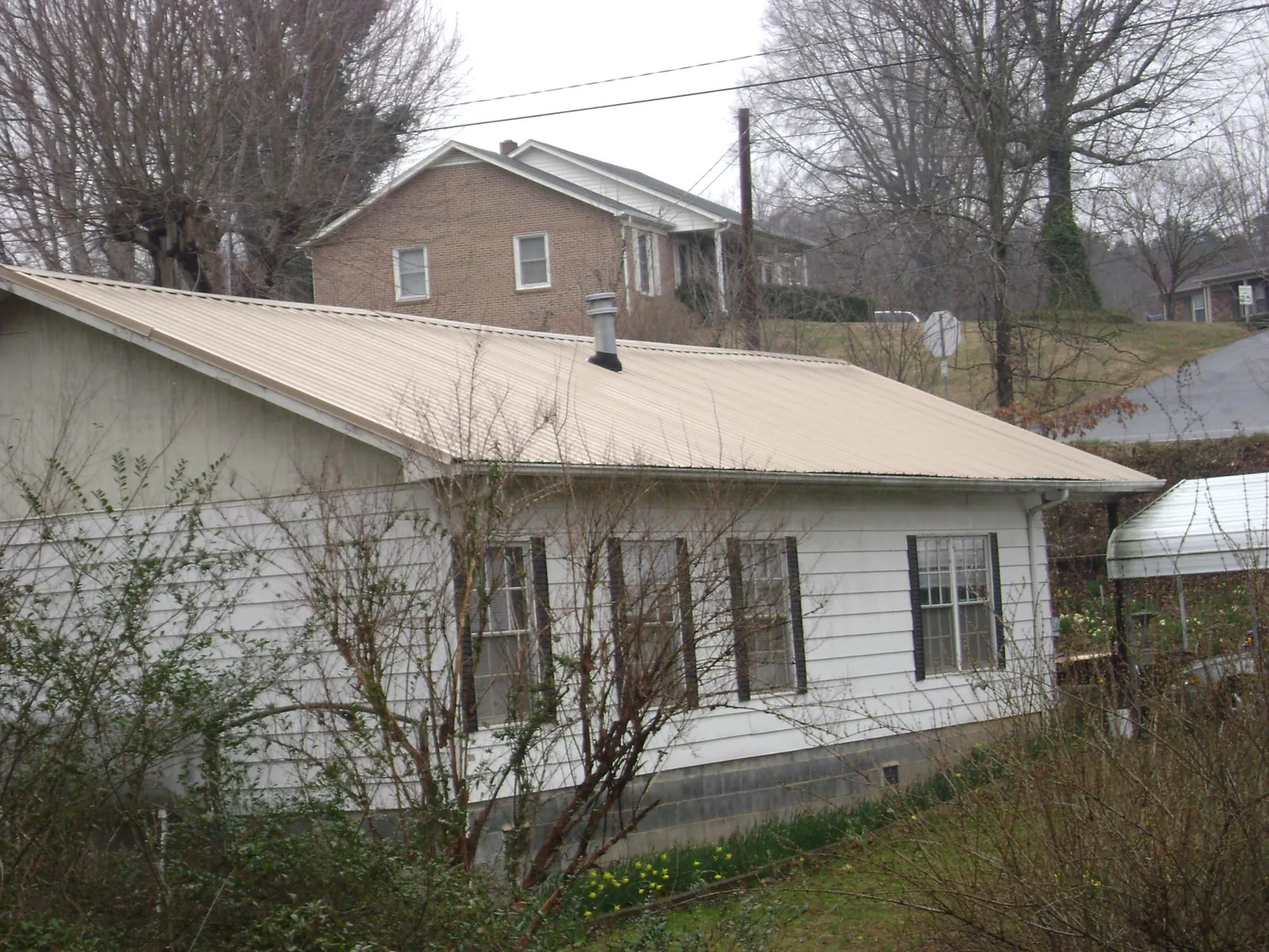 Tan metal roof on a white sided house set into a hillside — Commercial Roofing by Roofing Brothers in Haverford